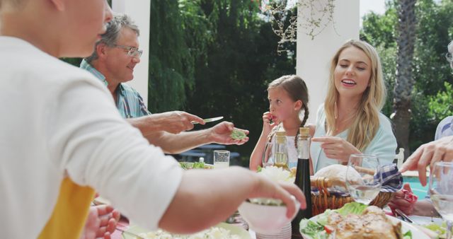 Happy caucasian family sitting at table in garden, eating dinner and talking. Lifestyle, domestic life, family, and togetherness.