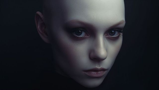 Bald female portrait staring intense gaze wearing dark high-collar top with porcelain skin