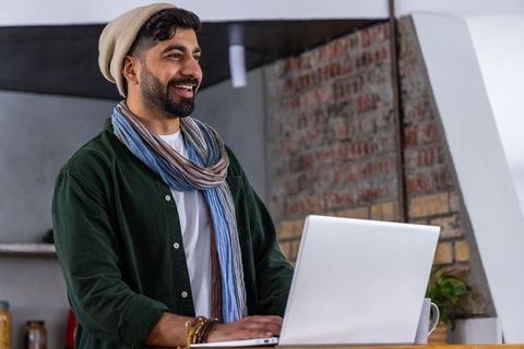 Young man working on laptop in cozy industrial loft wearing beanie and scarf