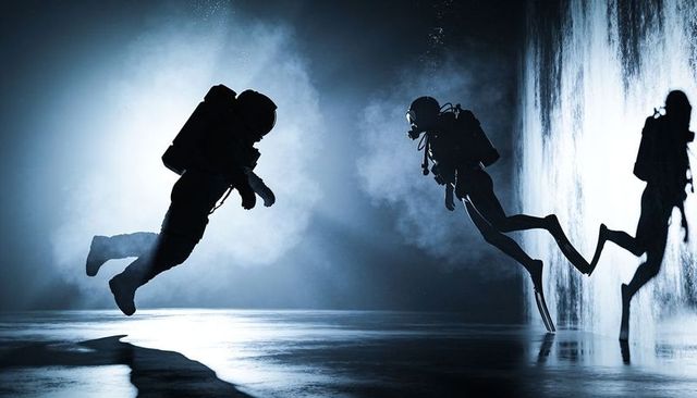 Scuba divers training in backlit misty tank, silhouette teamwork with regulators and fins