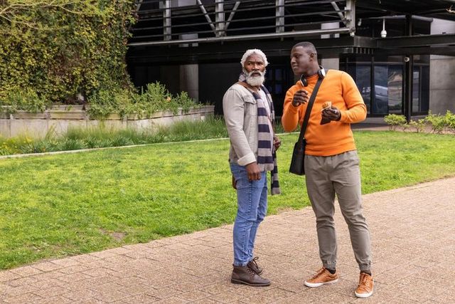 African american senior and young man chatting in urban courtyard holding sandwich
