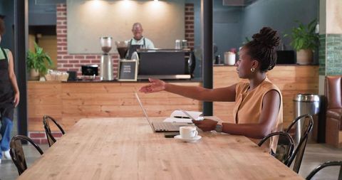 African american woman gesturing while working on laptop at rustic coworking cafe table