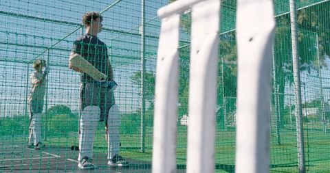 Young men practicing cricket batting in outdoor net cage during summer training session