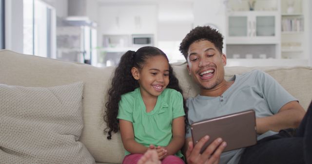Happy biracial father and daughter sitting on sofa using tablet - Download Free Stock Photos Pikwizard.com