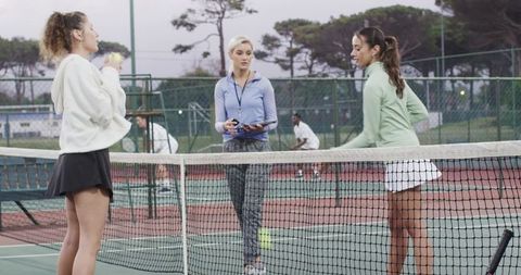 Female tennis players receiving coaching at net on outdoor court during practice session