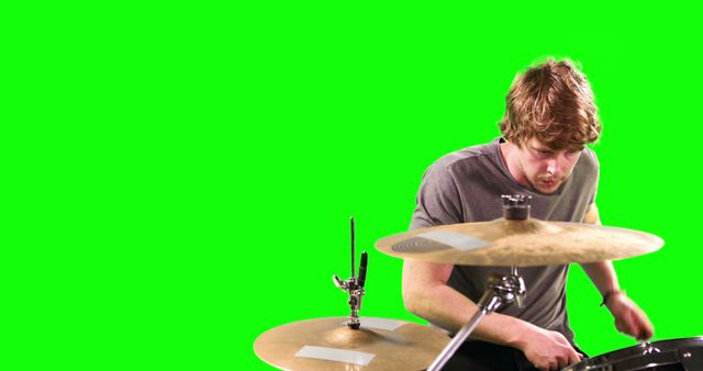 Young male drummer intensely focused on playing drum kit. Background features green screen, ideal for video and media editing. Suitable for use in comprehensive art projects, musical promotional materials, and design elements.