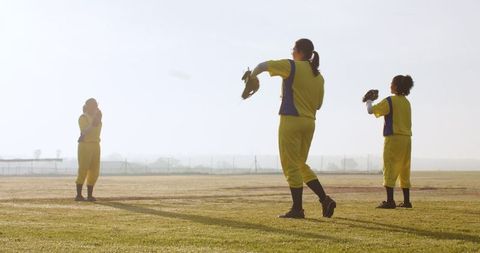 Diverse female team practicing softball at dawn in vibrant yellow uniforms