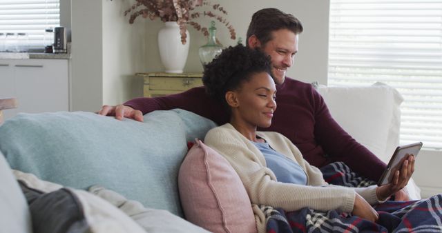 Image of happy diverse couple using tablet on sofa. Love, relationship and spending quality time together at home.