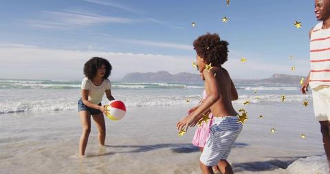Family playing beach ball at shoreline with children, sunny ocean waves and gold stars