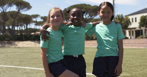 Smiling girls linking arms on sunny school sports field promoting teamwork and friendship