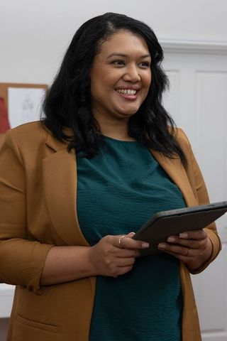 Confident businesswoman presenting and smiling while holding tablet in office meeting