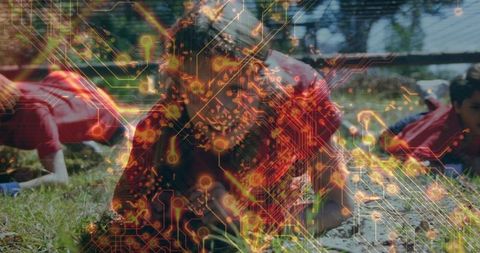 Children wearing red sportswear crawling under a net on a mud field while a circuit board overlay suggests innovation. This juxtaposition of adventure and technology can be used to represent teamwork, exploration, or the integration of traditional activities with modern technological themes.