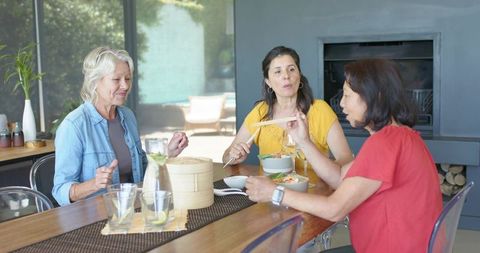 Mature diverse women sharing lunch, conversation at wooden table with bamboo steamer