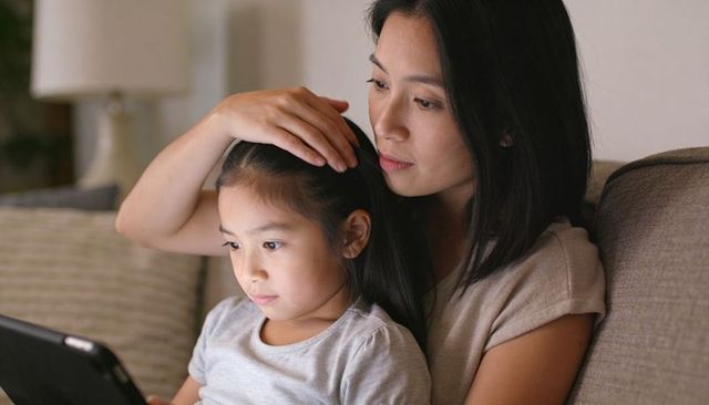 Mother bonding with daughter on sofa using tablet, cozy family night at home