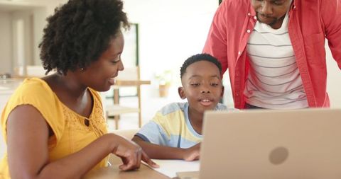 African American parents guiding son on laptop at sunlit kitchen table