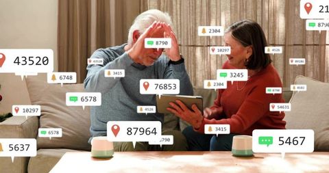 Senior couple reacting with delight to tablet notifications in cozy digital living room