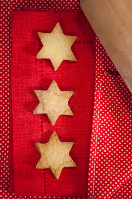 Three star-shaped cookies placed on a red polka dot napkin with a rolling pin nearby. Ideal for holiday-themed content, baking blogs, festive recipe illustrations, and Christmas greeting cards.