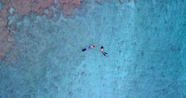 Aerial view of a diverse couple floating in clear blue waters. They enjoy a tranquil moment together in a serene outdoor setting.
