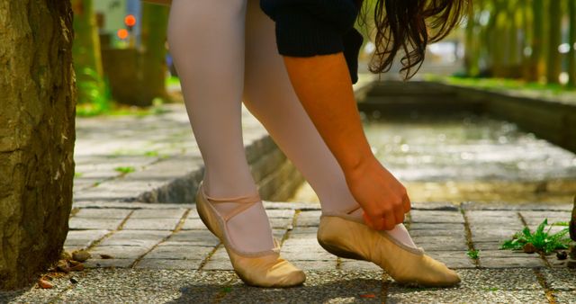 Low section of ballerina wearing ballet shoe in the park. Female ballerina sitting on stone bench 4k
