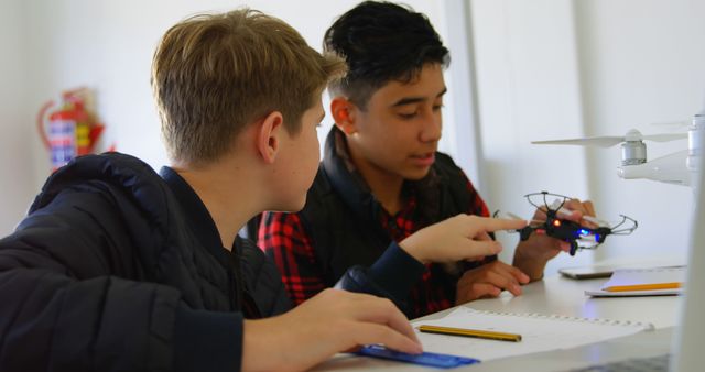 Two teenage boys are actively engaging in learning about drone technology during a classroom setting. They are using hands-on methods to understand the mechanics and applications of drones. This image can be used for educational websites, tech tutorials, STEM program promotions, and articles on innovative learning methods.