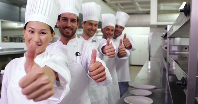 This image shows five chefs in professional kitchen uniforms giving thumbs up. They are standing in a line, indicating a strong sense of teamwork and collaboration. This can be used to represent themes such as teamwork, culinary arts, customer satisfaction, and professionalism in the restaurant industry. Ideal for culinary schools, restaurant promotions, cooking events, or articles on teamwork within hospitality sectors.