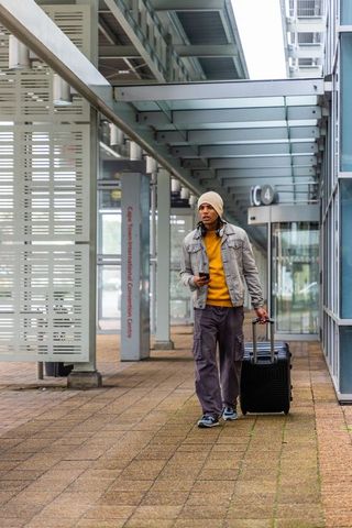 Traveler walking with rolling suitcase and phone under cape town convention centre canopy