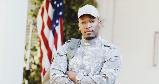 Military personnel posing confidently with arms crossed in front of American flag. Ideal for use in content promoting military service, Veterans Day events, patriotic themes, or recruitment campaigns.