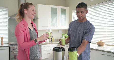 Couple making green smoothies in bright kitchen sharing healthy morning drinks and smiles