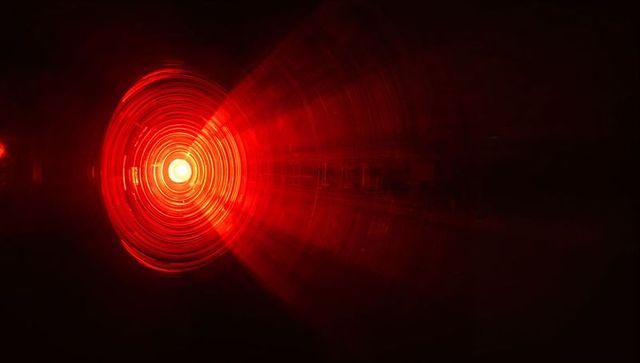 Emitting red circular light with concentric rings and radial beams in dark space