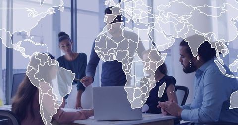 Diverse team collaborating over laptop with world map overlay in sunlit office meeting