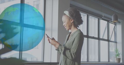 Businesswoman using smartphone with globe hologram in office