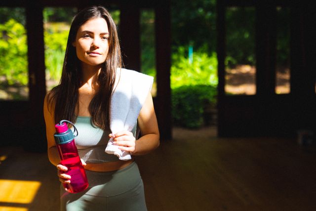 Portrait of caucasian young woman with napkin and water bottle in yoga studio, copy space. unaltered, fitness, yoga and healthy lifestyle.