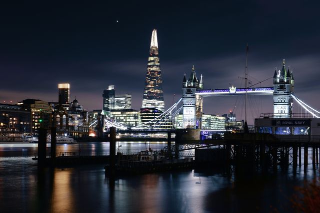 Tower Bridge and the Shard sparkling over the River Thames at night, iconic symbols of London. Suitable for travel publications, educational materials, website banners, or backgrounds depicting famous landmarks.