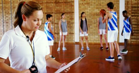 Female coach overseeing basketball practice in gym
