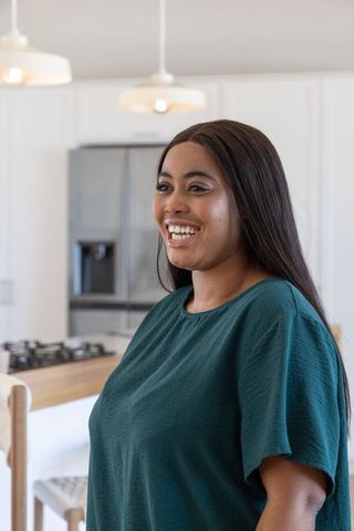 African american woman smiling and standing in bright modern kitchen wearing teal blouse