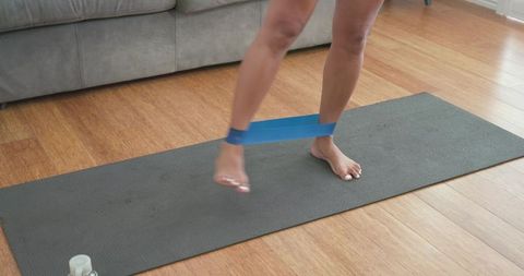 Woman performing lateral resistance band walk on yoga mat for glute and ankle strength