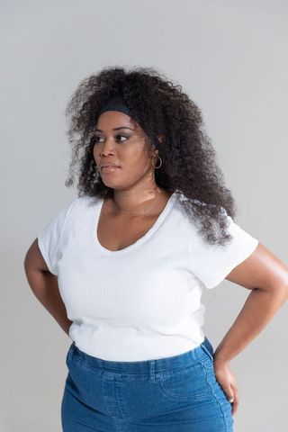 Confident african american woman posing hands on hips wearing white top and denim jeans