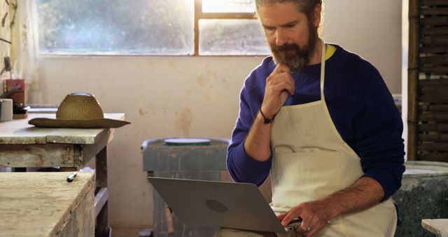 Bearded Artisan Wearing Apron Working on Laptop in Studio - Download Free Stock Images Pikwizard.com