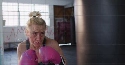 Determined woman boxer training with pink gloves against heavy bag with data overlay