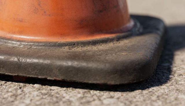 Close-up showing weathered orange traffic cone resting on concrete with rubber base