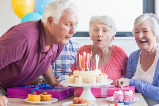 Seniors gathered around a table celebrating a birthday with a cake and candles. They are smiling and enjoying the moment, with gifts and balloons in the background. This image can be used for promoting senior living communities, retirement home activities, elderly care services, and celebrating special occasions with seniors.
