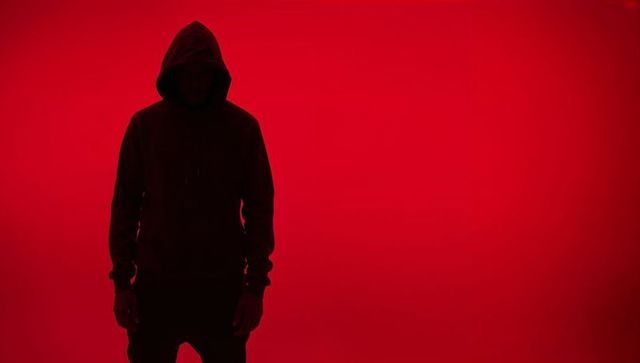 Anonymous hooded figure silhouetted against red background