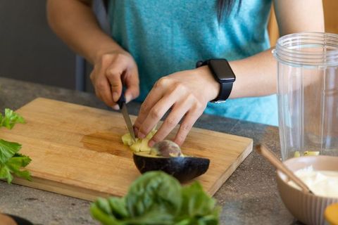 African american woman slicing fruit on cutting board while preparing avocado smoothie