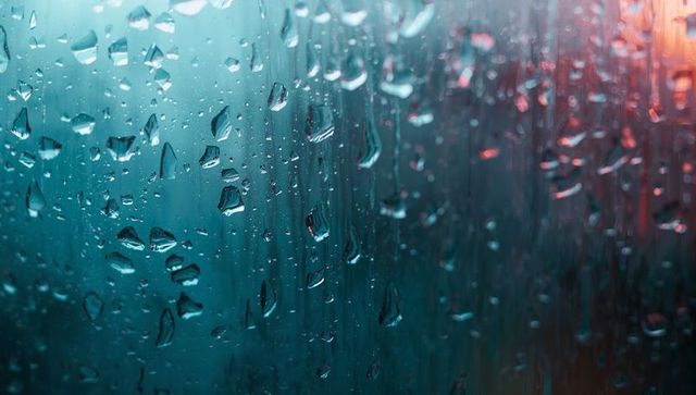Glistening rain on glass with soft ambient light reflections