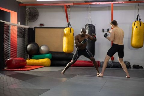 Black and white men sparring in mma gym training on padded mats with heavy bags