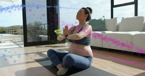 Expectant woman practicing prenatal yoga in sunlit living room on navy yoga mat