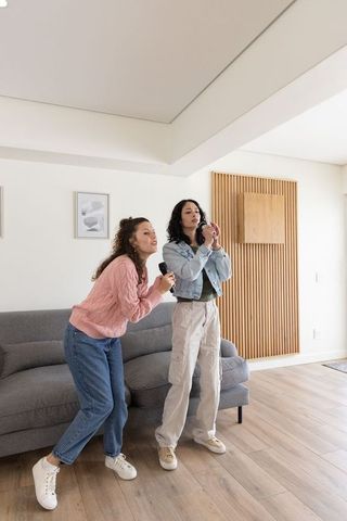 Two friends singing karaoke in modern living room holding microphones and phone
