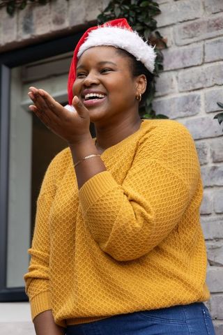 African american woman smiling and blowing kiss in santa hat and mustard sweater
