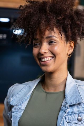 African american woman smiling in denim jacket and olive top, warm cafe headshot
