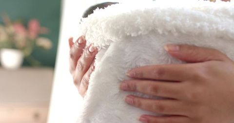 Soft female hands holding plush white faux fur throw in cozy bedroom
